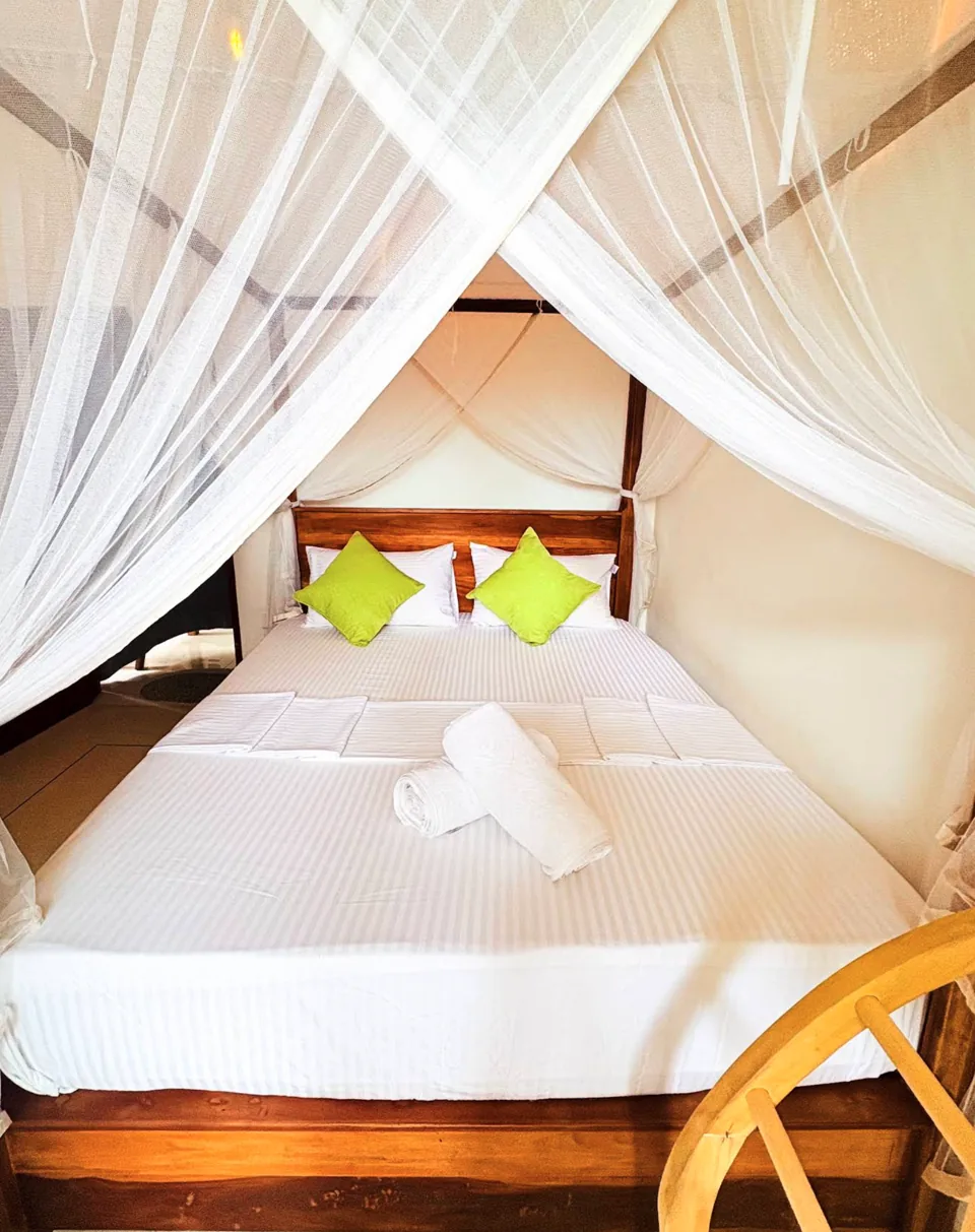 Double bed with a white mosquito net and green cushions at Ashen Surf House