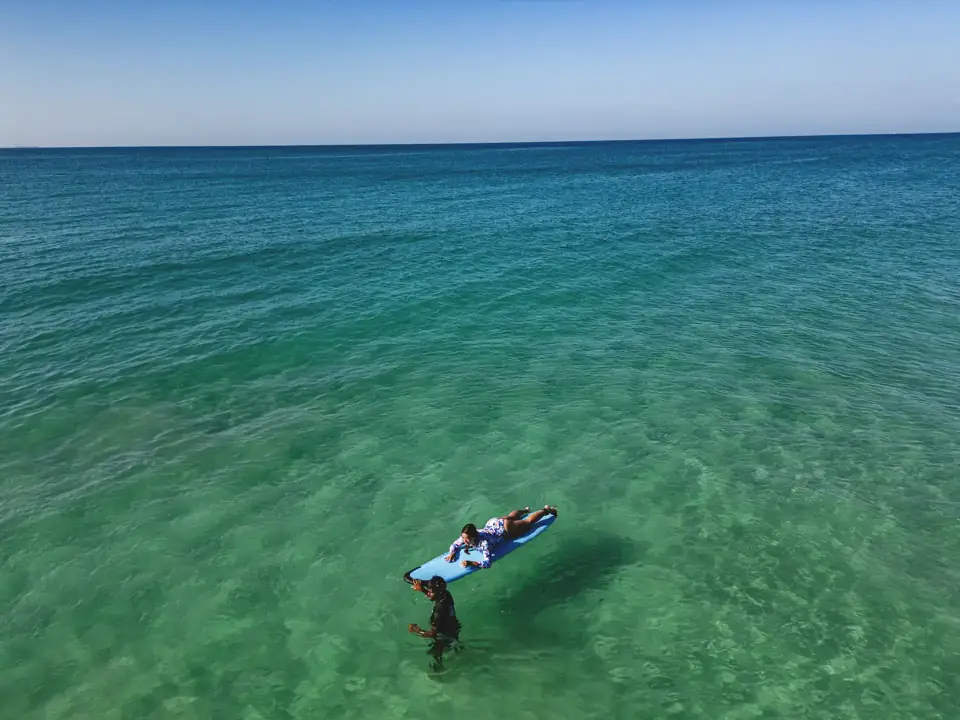 A surfer paddles into the clear green waves at Kabalana