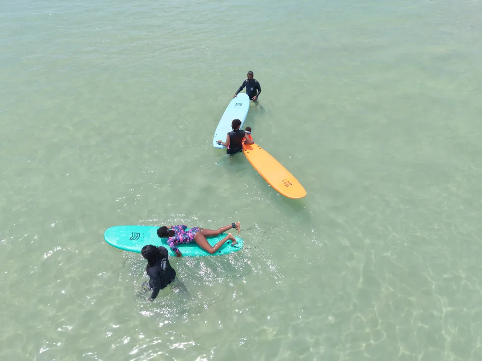 An Ashen instructor supports a surfer in the water at Kabalana